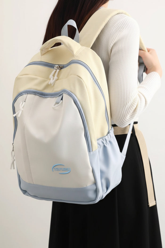 Beige and light blue backpack worn by a person on a white background