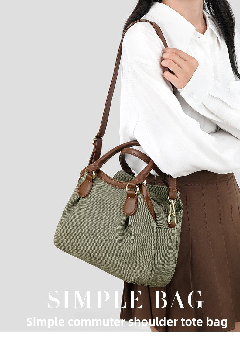 Green shoulder tote bag with brown straps held by a person wearing a white shirt and brown pants on a light gray background.