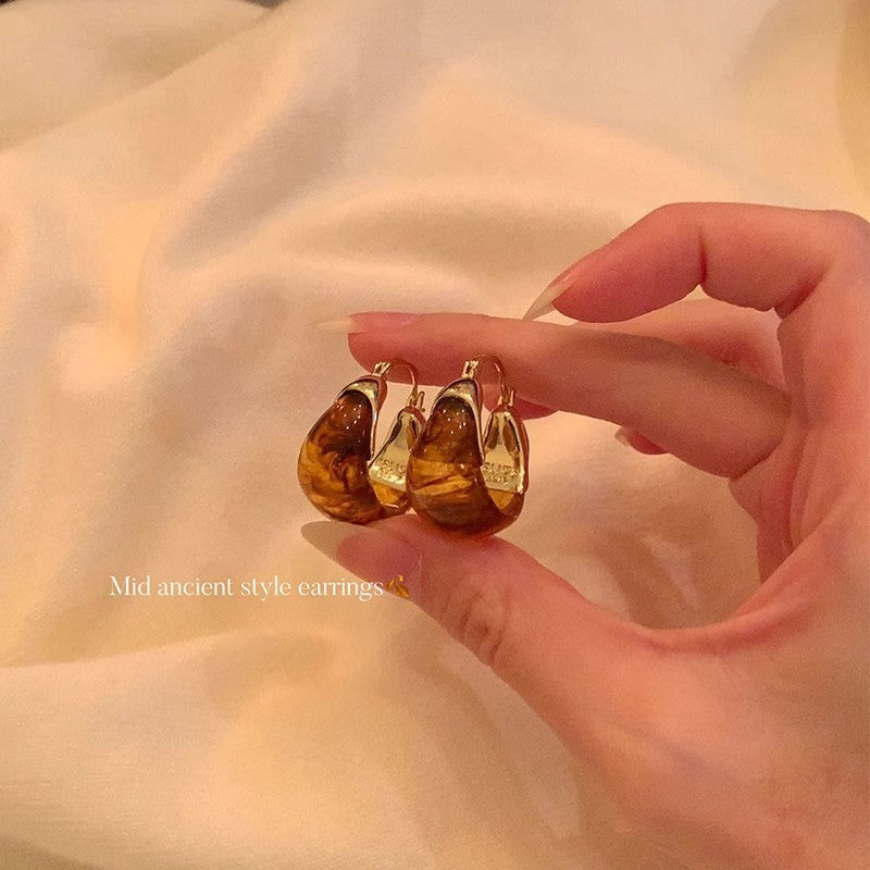 Hand holding amber teardrop earrings against a soft beige background