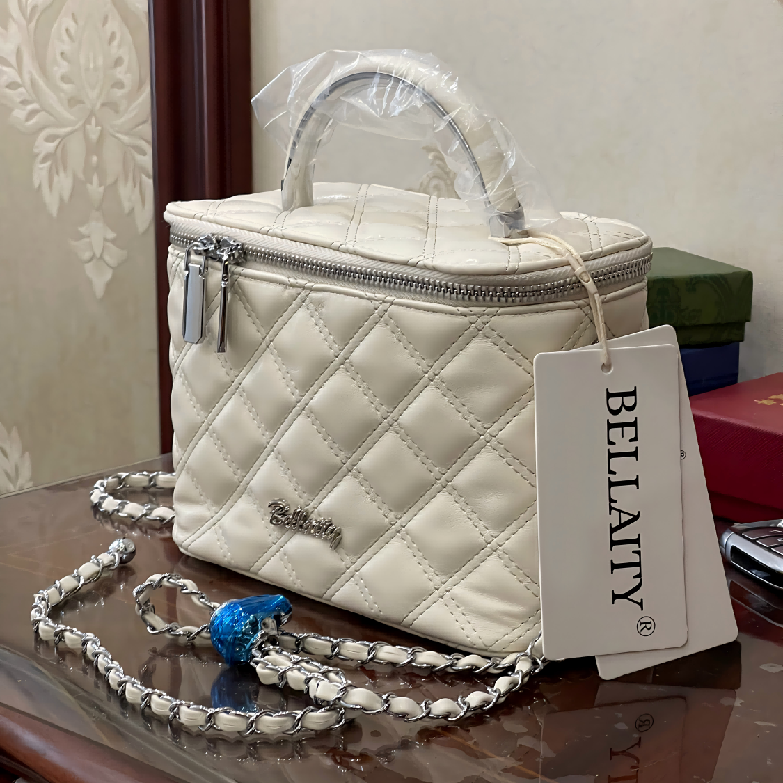 White quilted handbag with a chain strap and Bellacity tag on a reflective surface.