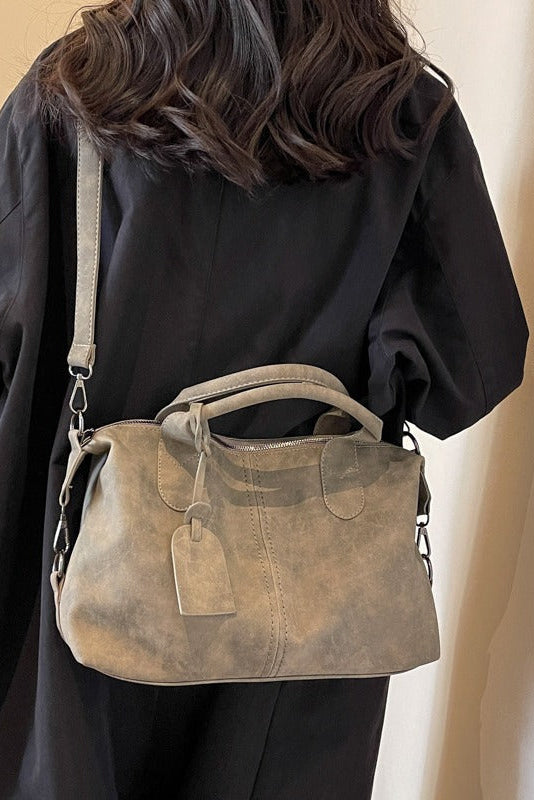 Person wearing a dark jacket with a brown leather handbag on a plain background